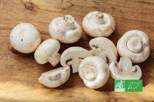 Champignons de Paris bio entiers et tranchés sur une planche en bois, avec logo AB